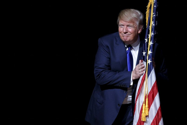 Trump ôm cờ Mỹ trên khán đài tại một sự kiện tranh cử ở Derry, New Hampshire Derry. (Ảnh: Brian Snyder/Reuters)