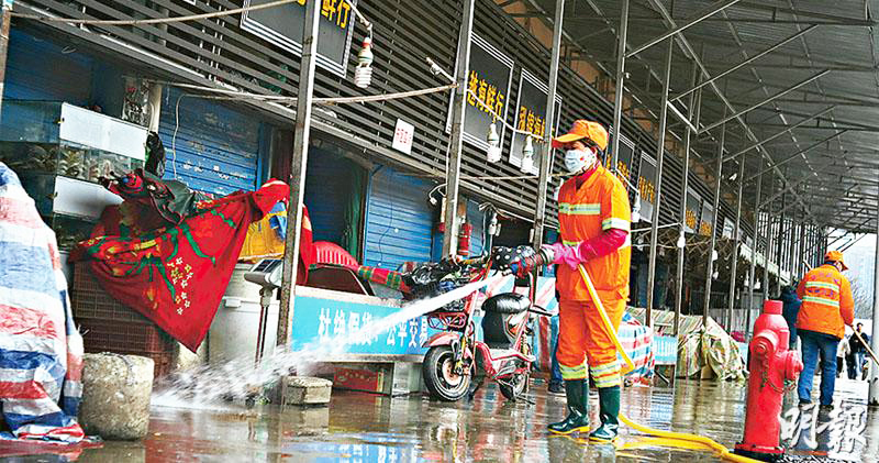 tại chợ hải sản Hoa Nam, các nhân viên mặc quần áo phòng cháy chữa cháy màu trắng đang phun thuốc vào cửa của nhiều cửa hàng và cổng sắt ở hai bên hành lang.